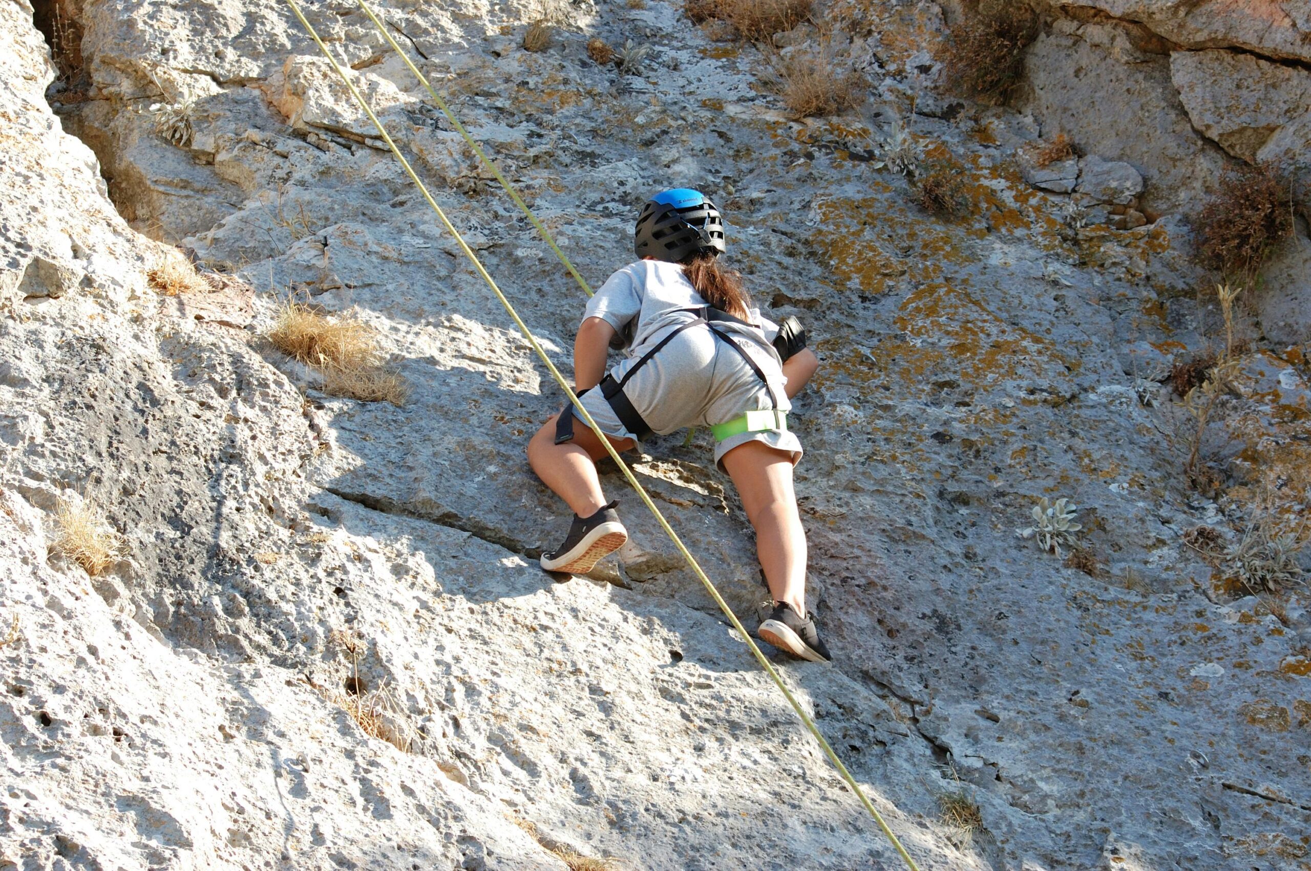 Female rock climber scaling a rocky cliff, showcasing outdoor adventure and skill.